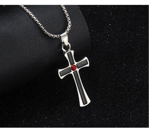 Macro shot of black and silver cross pendant with red gemstone on a metal chain