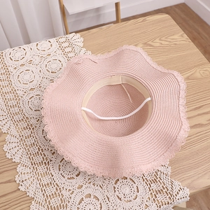 Détail du chapeau de paille rose avec bords ondulés et sangle sur fond dentelle