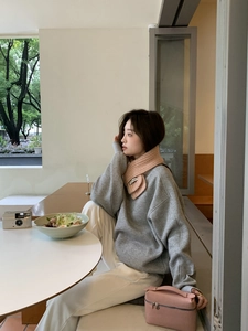 Close-up of a pink knitted scarf worn with a gray crewneck sweatshirt in a bright cafe setting