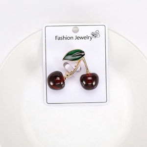 Detailed close-up of glossy deep red cherry brooch with green leaf on a card