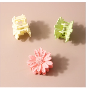 Close-up of three daisy hair clips in pink, light green, and beige with metal springs