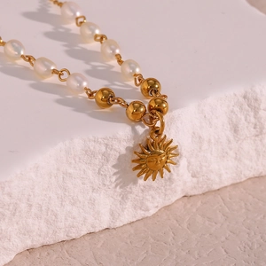 Macro detail of golden sun pendant with freshwater pearl and metallic bead chain