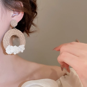 Detail of woven straw hoop earrings featuring white fabric flowers and center pearls