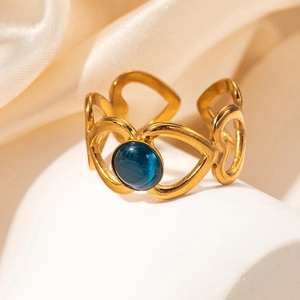 Gros plan d'une bague coeur dorée ajourée avec pierre oeil de chat bleue sur soie