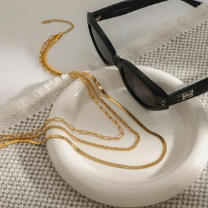 Close-up of triple-layered gold titanium steel necklaces on a white ceramic plate