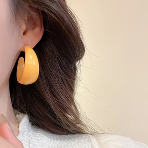 Close-up of a minimalist orange acrylic C-shaped earring on model with glossy finish