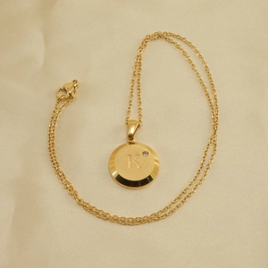 Macro detail of 18K gold-plated necklace with brushed metal round letter K pendant
