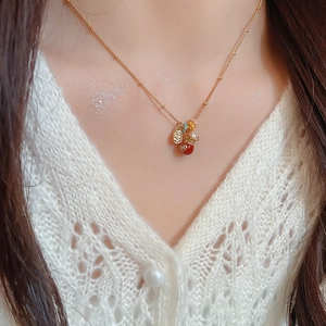 Detail of gold-plated necklace with lucky pouch pendant, pearls and red beads on model