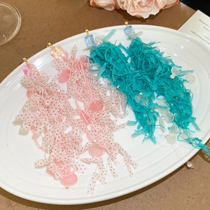 Detailed view of pink and teal fabric floral tassel earrings on a white ceramic tray
