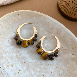 Macro shot of gold C-shaped earrings set with five tiger eye stones on ceramic plate