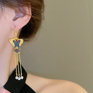 Detail of gold butterfly tassel earrings with enamel butterfly and white bead pendants