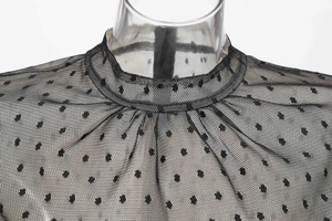 Detail of sheer black mesh dress with polka dots and high collar on transparent mannequin