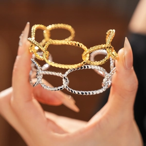 Close-up of gold and silver irregular oval hollow bangles worn on a wrist in soft light