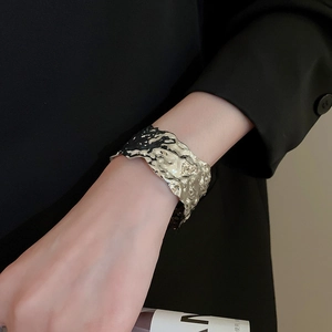 Detailed view of broad silver metal cuff bracelet featuring irregular hammered textures