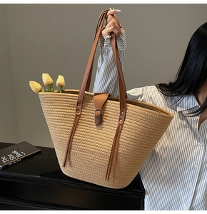 Close-up of khaki woven straw tote bag with brown leather handles and tassel detail