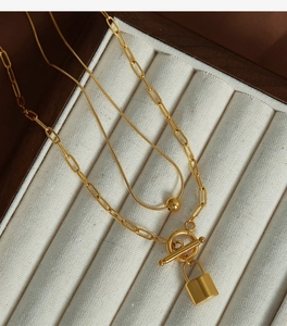 Detailed macro view of a gold-toned double-layered necklace with lock pendant and OT clasp