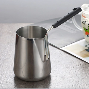 Polished stainless steel Turkish coffee pot with long black handle on textured surface