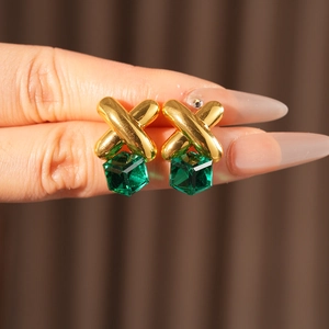 Close-up of vintage gold cross earrings with emerald green cube gemstones held in hand