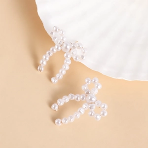 Close-up of handmade white pearl bow earrings with gold wire detail on a shell