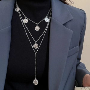 Close-up of layered silver coin pendant necklace styled on a black turtleneck sweater