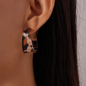 Detail of a C-shaped leopard print acrylic hoop earring worn on a model's ear lobe