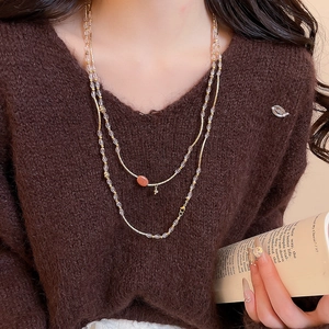 Detail of a double-layered crystal beaded necklace with a brown stone pendant on a model