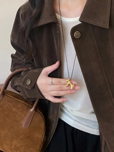 Detail of golden horse pendant necklace worn over a vintage brown suede jacket