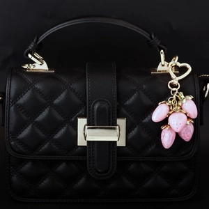Close-up of pink strawberry charm on black quilted PU leather handbag with gold hardware