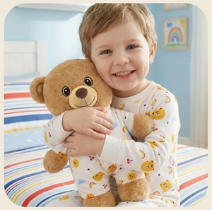 Smiling child holding a brown teddy bear with colorful cartoon patterned baby pajamas