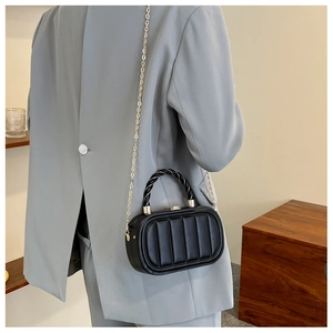 Detail of black quilted box bag with woven handle and gold chain on a grey blazer