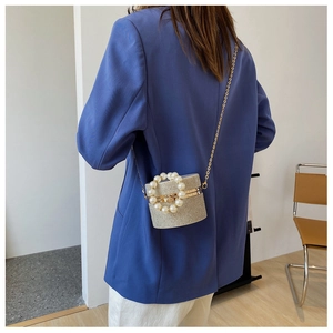 Detailed view of silver rhinestone bucket bag with pearl handle and metal chain on blue suit