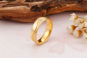 Détail d'une bague dorée avec rainure chevron et trois zircons sur fond de bois et fleurs