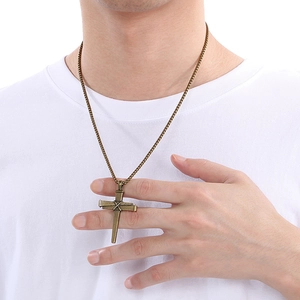 Gros plan d'un pendentif croix en clous de bronze porté sur une chaîne en métal