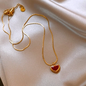 Elegant gold snake chain necklace featuring a glossy red heart pendant on silk background