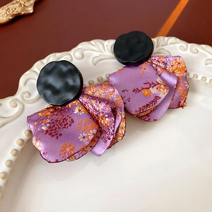 Detail view of purple floral fabric earrings with black irregular studs on a ceramic tray