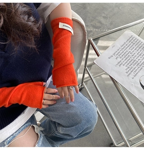 Close-up of bright orange knitted fingerless gloves with white woven more moment label