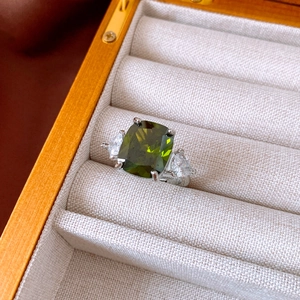 Detail of an olive green cushion-cut zircon ring with teardrop side stones in a wood box