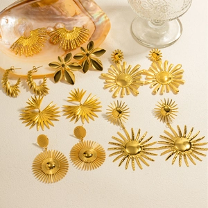 Macro detail of 18k gold plated sunflower earrings and luxury sunburst charms on textured background