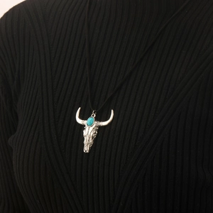 Detailed view of silver bull skull pendant with turquoise stone on black knit fabric
