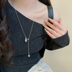 Close-up of elegant Y-shaped necklace with baroque pearl and silver ball pendant on model