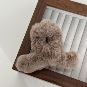 Close-up of soft khaki plush hair claw clip with fluffy texture on a wooden display stand