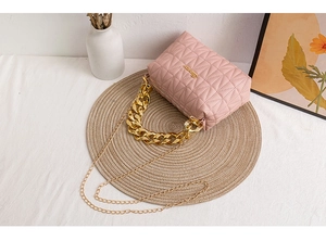 Pink quilted crossbody bag with gold chain strap and heavy top handle on a woven mat