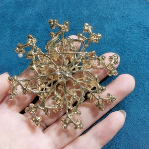 Golden snowflake brooch with faux pearls held over a blue velvet background