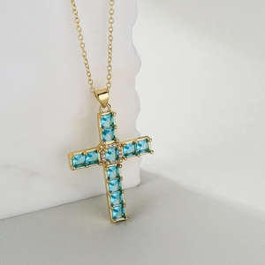 Minimalist gold-plated cross necklace with light blue zircon stones on textured stone
