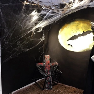 Halloween decor setup with black cross, creepy spider web, and wall bat silhouettes