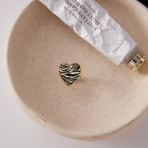 Detail of 18K gold heart zebra print ring on a ceramic tray with lifestyle aesthetics