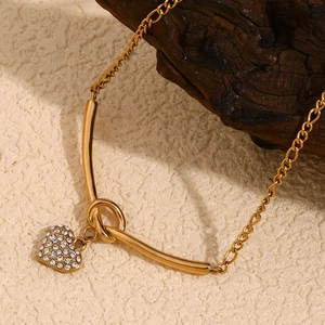 Détail macro d'une chaîne Figaro plaquée or 18K avec barre en V nouée et pendentif coeur