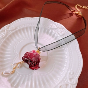 Close-up of red rose pendant with pearl tassels on a black lace choker necklace