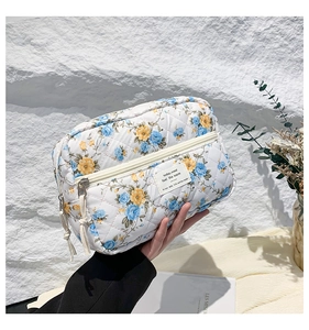 Close-up of quilted floral makeup bag with blue rose patterns and tassel zipper detail