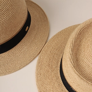 Close-up of premium raffia fedora with black ribbon and gold logo hardware detail